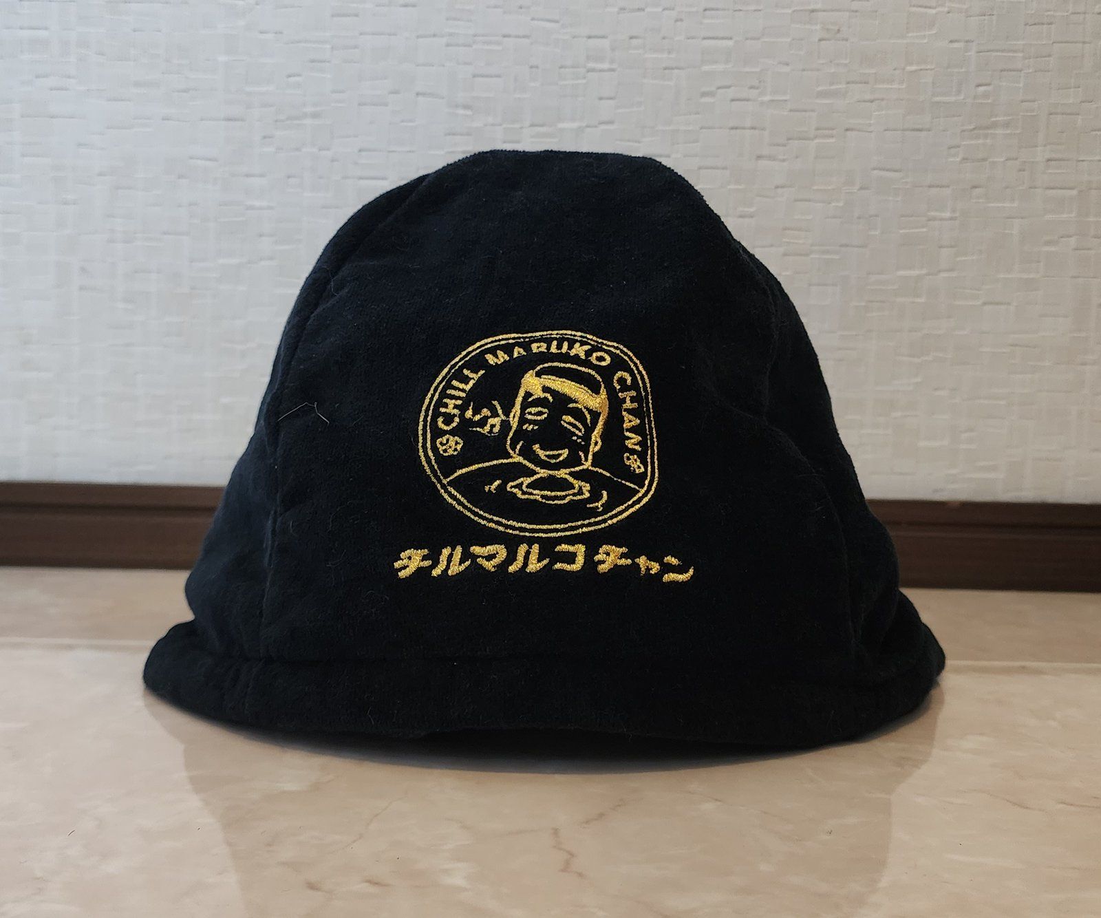 チルマルコチャン今治タオルサウナハットの正面。黒地に金の刺繍でお風呂につかったヒロシとロゴが入っている